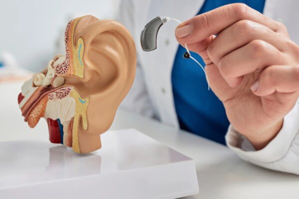 Anatomický model ľudského ucha a ruka lekára držiaca moderný digitálny načúvací prístroj.