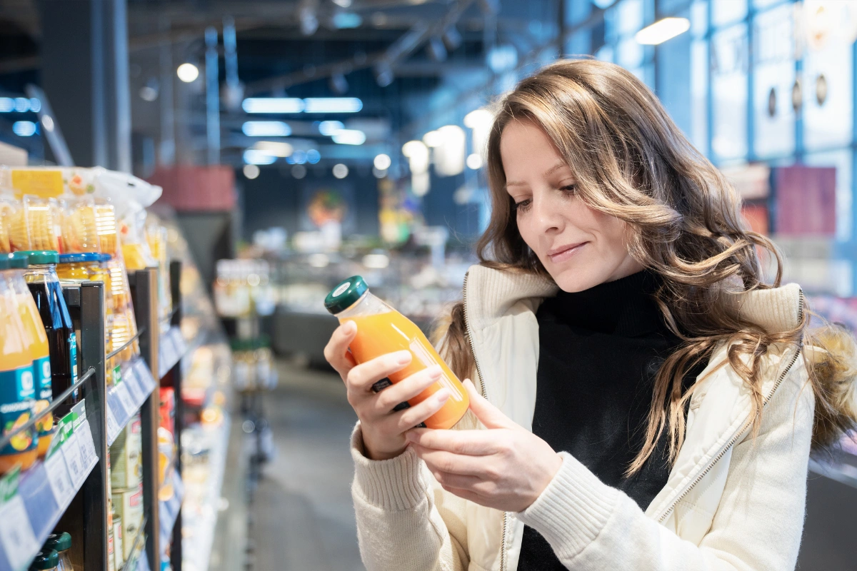 Mladá žena v supermarkete číta zloženie na fľaši džúsu, aby si overila kvalitu kupovanej potraviny.