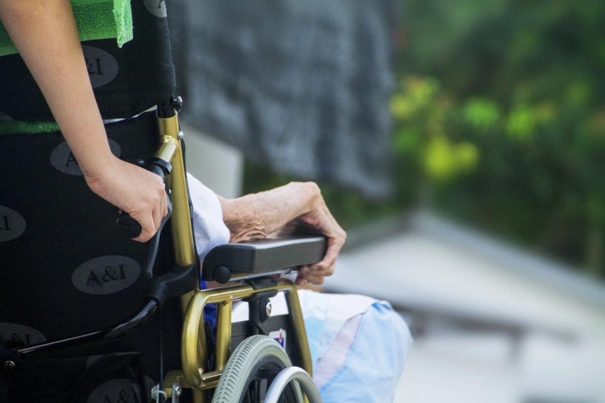 Opatrovateľ tlačí invalidný vozík s imobilnou osobou – starostlivosť a prevencia preležanín.